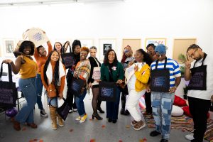 Attendees of the Therapeutic Spaces Welcome Party, hosted by Artist Talk Mental Health, pose for a group photo with tote bags they screen printed during the event. Photo courtesy of Sydney Davis.